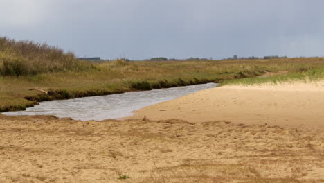 wide-shot-of-sandy-tidal-inlet-stream-running-on-to-the-beach,-on-at-mud-flats,-Saltfleet,-Louth,-Lincolnshire