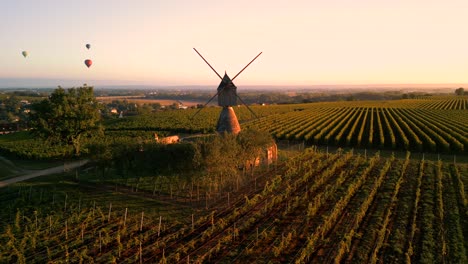 Eine-Wunderschöne-Vogelperspektive-Auf-Französische-Weinberge-In-Der-Goldenen-Abendsonne-Mit-Luftballons-Am-Himmel-Und-Einer-Historischen-Windmühle