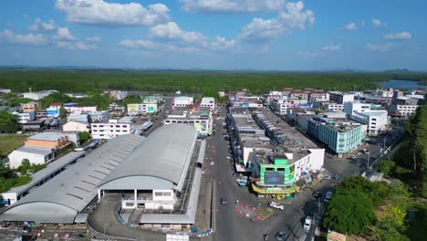 Great-aerial-view-flight-of-krabi-town-market-hall-in-southern-thailand,-showing-a-mix-of-buildings,-a-river,-the-sea,-and-forested-hills-in-the-background