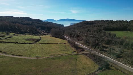 Los-Verdes-Campos-De-La-Región-De-Tavertet-Y-La-Sinuosa-Carretera-Con-Montañas-En-La-Distancia,-Vista-Aérea