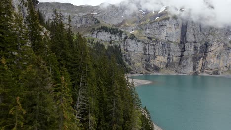 Aerial-take-of-The-Oeschinen-blue-lake-in-Switzerland,-surrounded-by-trees