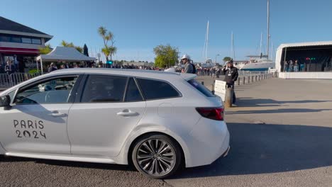 El-Coche-De-París-2024-Pasa-Lentamente-Con-Las-Luces-Encendidas-Y-Seguridad-A-Su-Alrededor.