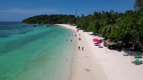 Touristen-Genießen-Einen-Sonnigen-Tag-An-Einem-Tropischen-Inselstrand-Mit-Traditionellen-Thailändischen-Longtail-Booten,-Die-Im-Türkisfarbenen-Wasser-Vertäut-Sind