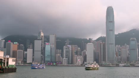 Against-the-backdrop-of-Hong-Kong-Island's-urban-skyline,-Star-Ferries-traverse-Victoria-Harbour,-showcasing-the-iconic-skyscrapers-of-Hong-Kong-Island's-financial-district