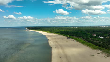 Aerial-Stogi-Beach,-showcasing-a-long-stretch-of-sandy-shoreline-bordered-by-lush-green-forests-and-calm-blue-waters