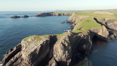 An-aerial-view-of-Abereiddi-Tower-in-Pembrokeshire,-South-Wales,-on-a-sunny-evening-with-a-clear-blue-sky