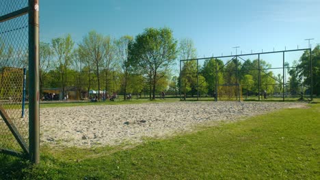 Sunny-day-at-Jarun-Lake-in-Zagreb,-Croatia,-featuring-a-sandy-volleyball-court-surrounded-by-green-trees-and-grassy-areas