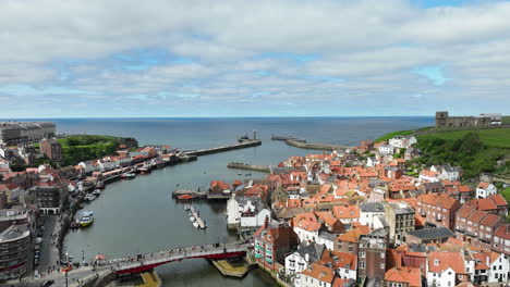 Whitby-harbor-with-boats-and-red-roofed-buildings-under-a-partly-cloudy-sky,-aerial-view,-hyperlapse