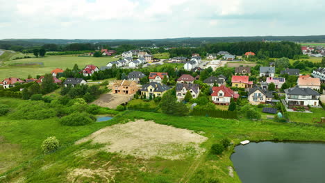 Vista-Aérea-De-Una-Zona-Residencial-En-Un-Entorno-Rural-Con-Casas-Recién-Construidas,-Zonas-Verdes-Y-Un-Pequeño-Estanque.