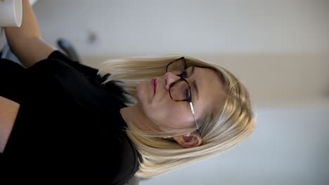 A-vertical-video-captures-a-female-office-worker-seated-at-her-desk,-panning-across-different-monitor-screens,-illustrating-the-concept-of-multitasking-in-a-modern-workplace