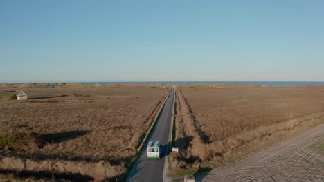 Drone-footage-of-a-coastal-road-stretching-through-fields-towards-the-ocean-on-a-clear-day