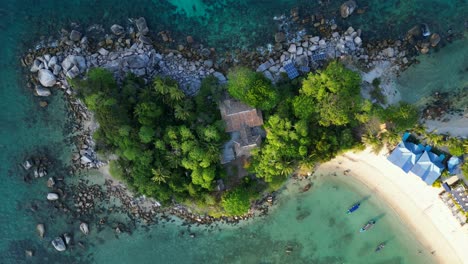 Magic-aerial-view-flight-of-a-Hut-on-a-tropical-Sole-peninsula-with-turquoise-water-and-lush-green-vegetation,-surrounded-by-a-coral-reef,-variety-of-marine-life