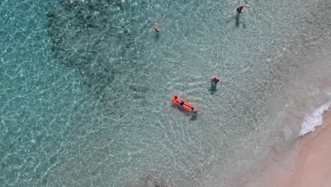 Vista-Cenital-Desde-Arriba-Con-Drones-De-Personas-Relajándose-En-Aguas-Cristalinas-Azules-En-Una-Playa-Dorada-En-Menorca,-España