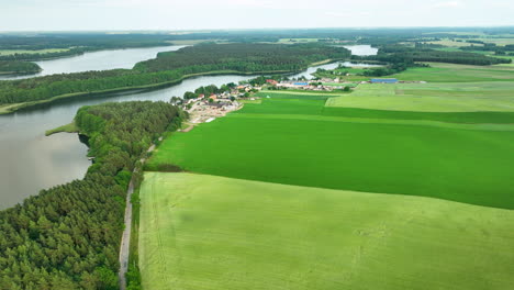 Vista-Aérea-De-Un-Paisaje-Rural-Con-Exuberantes-Campos-Verdes,-Un-Río-Sinuoso-Y-Un-Pequeño-Pueblo