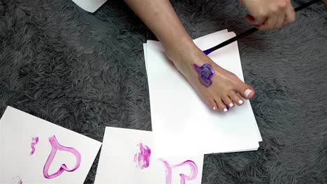 Tan-female-foot-print-is-created-on-white-paper-as-hand-uses-long-black-paintbrush-to-outline-with-paint