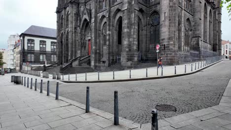 Street-view-with-pedestrians-passing-black-volcanic-Cathedral-Notre-Dame-of-Assumption-in-France