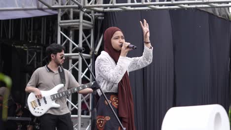 Indonesische-Muslimische-Sängerin-Mit-Hijab-Singt-Auf-Der-Bühne-Mit-Gitarrist-Im-Hintergrund-Während-Einer-Musikshow