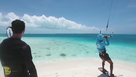 Instructor-De-Kitesurf-Prepara-Al-Hombre-Para-Saltar-Sobre-El-Agua-De-Mar-Azul,-Isla-De-Los-Roques