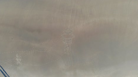 Aerial,-descending,-drone-shot,-of-a-water-tower-drawing-in-sand,-at-a-beach,-in-Langeoog,-Germany