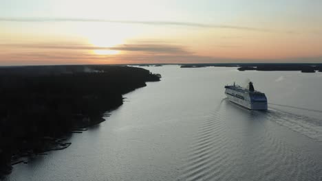 A-passenger-ferry,-heading-towards-an-orange-and-pink-sunset-in-the-Swedish-archipelago,-making-waves-in-the-calm-water-as-it-makes-it-way-in-between-islands