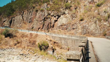 Car-going-down-hill,-through-road,-over-bridge-between-rock-country-cliffs-4K