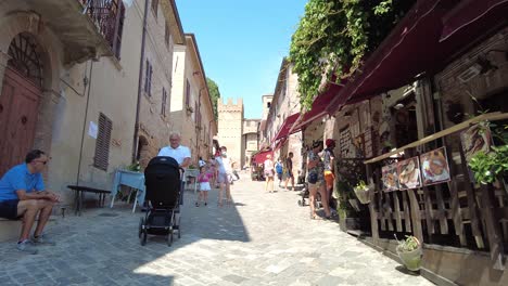 Tilt-down-reveal-shot-of-people-walking-on-cobblestone-street-in-Gradara,-Italy