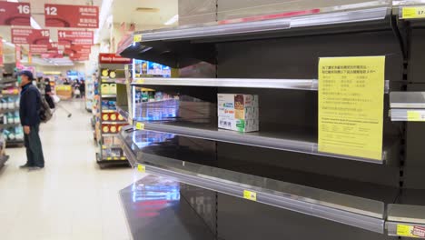 Shoppers-wear-face-masks-walk-past-empty-supermarket-shelves,-usually-stocked-with-toilet-paper