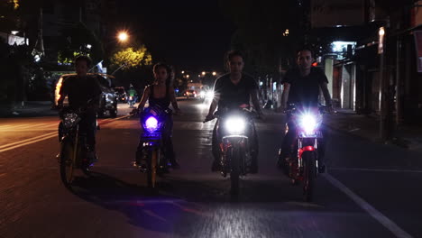 Tracking-shot-of-a-young-Asian-motorcycle-gang-with-male-and-female-riders,-driving-down-the-city-streets-of-Yogyakarta,-Indonesia-at-night