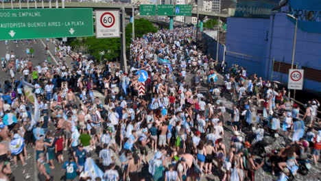 Flyover-shot-of-highway-crowded-with-football-soccer-argentinian-fans,-walking,-waving-flags,-some-of-them-climb-over-a-sign-during-celebration-of-world-cup