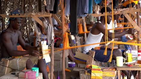 Tejedores-Expertos-Trabajan-Rápidamente-En-Telares-De-Madera-En-Ghana,-África-Occidental,-Tejiendo-La-Colorida-Tela-Kente-Para-La-Ropa-Tradicional-Africana