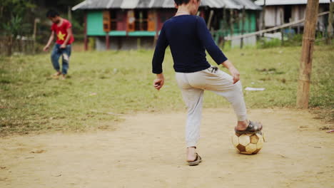 Young-Vietnamese-boys-play-soccer-outside-on-dirt-and-grass-ground,-slow-motion