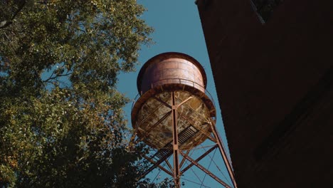 Alta-Y-Antigua-Torre-De-Agua-Rústica-Revelada-Desde-Detrás-De-Un-Gran-Edificio