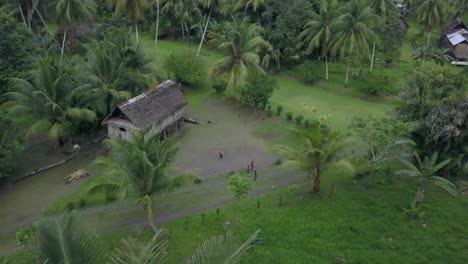 Vista-Aérea-En-Movimiento,-Niños-Reuniéndose-Y-Jugando,-Cabaña-Y-Palmeras-En-El-Fondo-En-La-Aldea-De-Kanganaman,-Región-De-Sepik,-Papua-Nueva-Guinea