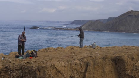 Fishermen-fishing-in-Praia-de-Aljezur-beach-sea-cliff-edge,-in-Portugal