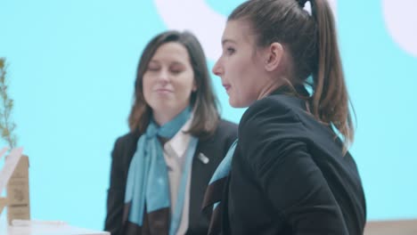 Shot-of-two-young-female-coworkers-standing,-talking-at-trade-show-event