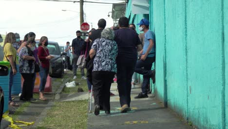 San-JosÉ,-Costa-Rica---6-De-Febrero-De-2022:-Editorial-Del-Día-De-Las-Elecciones,-Un-Hombre-Que-Lleva-A-Una-Anciana-A-Una-Cola-Fuera-De-La-Mesa-De-Votación,-Con-Gente-Haciendo-Cola