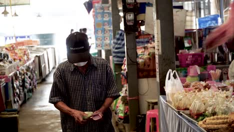 Static-Shot-of-Thai-Old-Man-Wearing-a-Face-Mask-due-to-Coronavirus-Outbreak-waiting-for-his-Change-in-a-Cover-Market-in-Bangkok