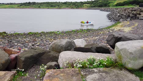 Fishermen-in-small-boat-landing-in-a-rocky-shore-in-Fife-Scotland-pulling-it-onto-the-beach