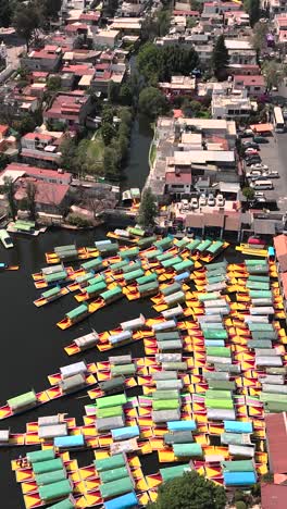 Perspectiva-Aérea-De-Los-Canales-De-Xochimilco-Mientras-Las-Trajineras-Navegan-Elegantemente-A-Través-De-Ellos,-Modo-Vertical