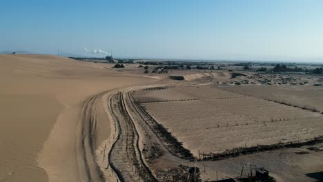 Campo-De-Cultivo-Seco-En-El-Desierto-Con-Tejido-Industrial-En-El-Fondo,-Vista-Aérea-De-Drones