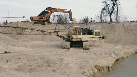 Aerial-dolly-out-view-of-an-abandoned-crane-on-the-bank-of-a-lake-on-a-bright-day