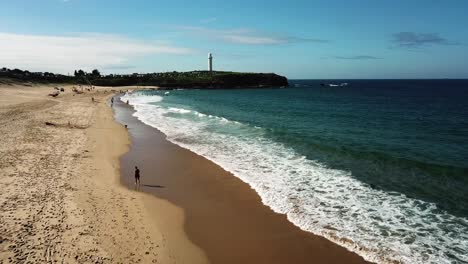 Aerial-drone-footage-of-sandy-beach-in-Australia-with-the-Light-House-of-Wollongong-in-far-distance