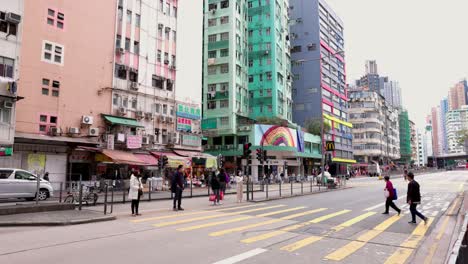 Multiple-Asian-people-walking-over-the-pedestrian-crossing-while-the-traffic-light-is-still-on-red-in-To-kwa-wan-in-Hong-Kong-between-the-high-colorful-appartment-buildings