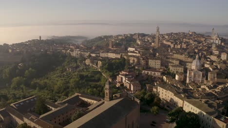 Slow-drone-flyover-medieval-church-in-foreground-to-reveal-city-of-Siena,-Italy-in-background