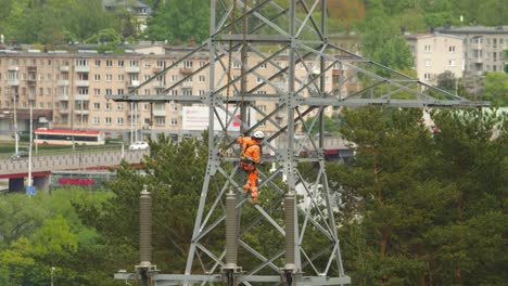 The-worker-climber-climbs-on-a-high-voltage-pole-that-is-being-prepared-to-be-lifted-by-a-crane