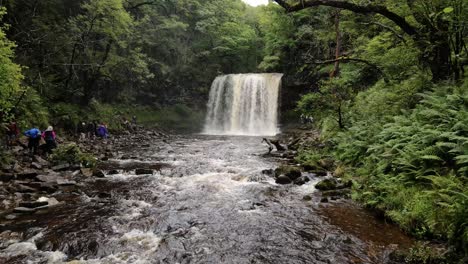 Tourists-sightseeing-cascading-Breacon-Beacons-idyllic-Welsh-uncultivated-waterfall-wilderness-aerial-reverse-shot