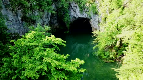 Aerial-view-of-Cerknica-Cave,-Slovenia,-with-a-river-flowing-in,-surrounded-by-a-forest