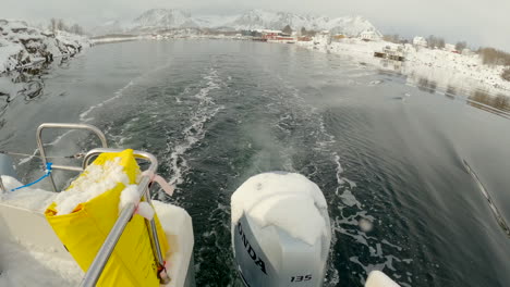 Schwenkbare-Aufnahme-Von-Einem-Außenbordmotor-Auf-Ein-Kleines-Schneebedecktes-Und-Friedliches-Dorf-Im-Norden-Norwegens-Am-Ufer-Einer-Kleinen-Bucht