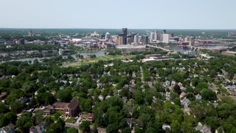 Wide-aerial-shot-slowly-tilting-downwards-with-the-city-of-Saint-Paul,-Minnesota-on-the-horizon-next-to-the-Mississippi-river-surrounded-by-trees-and-houses-on-a-sunny-day