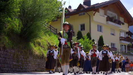 A-marching-band-dressed-in-traditional-Tyrolean-costumes-is-walking-towards-the-camera,-playing-music